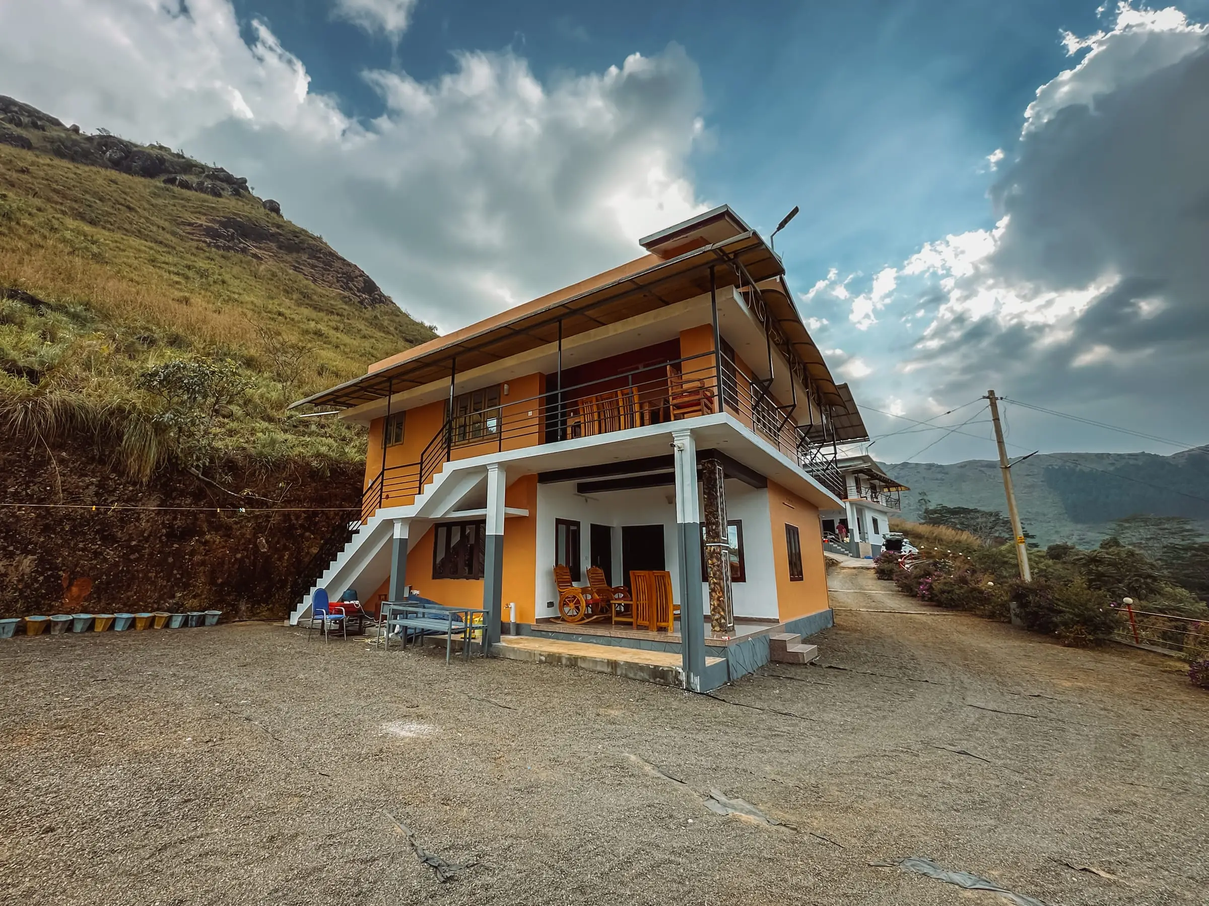 The two-storey home on its hillside terrace under a dramatic sky, with the valley behind