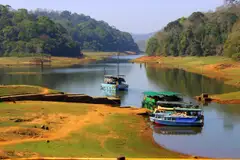 Tourist boats moored at a jetty on a lake with forested hills behind.