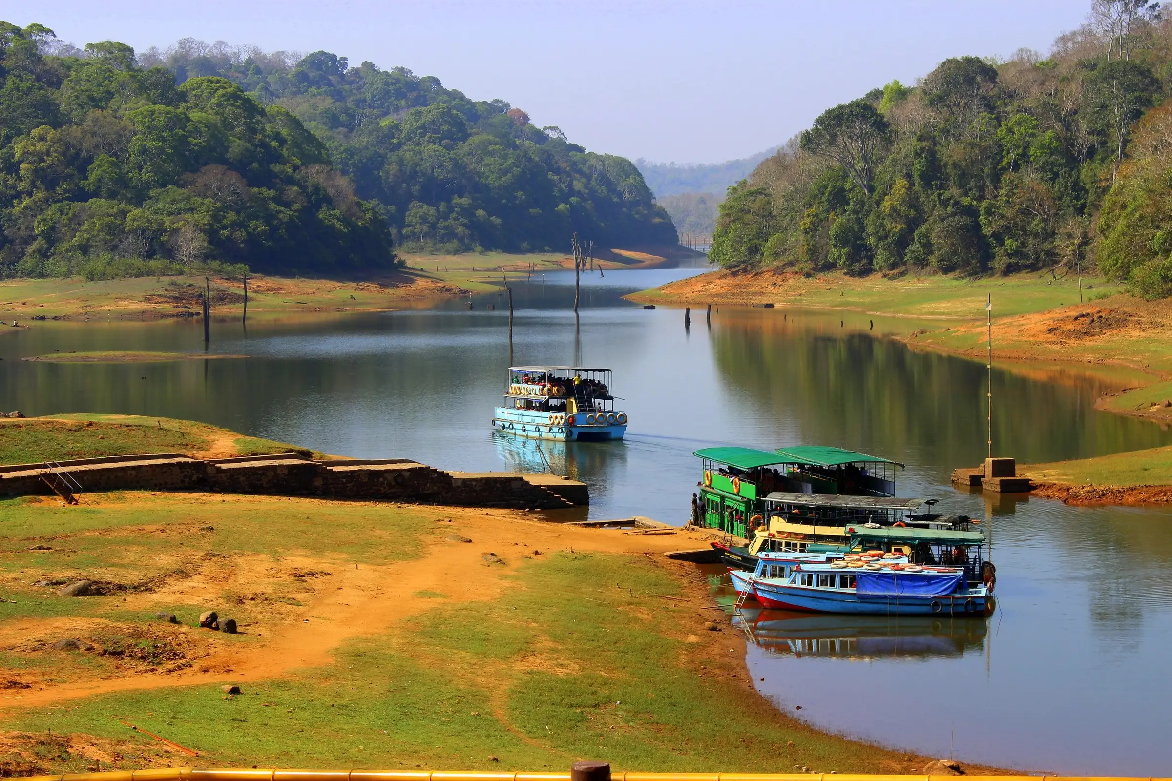Tourist boats moored at a jetty on a lake with forested hills behind.